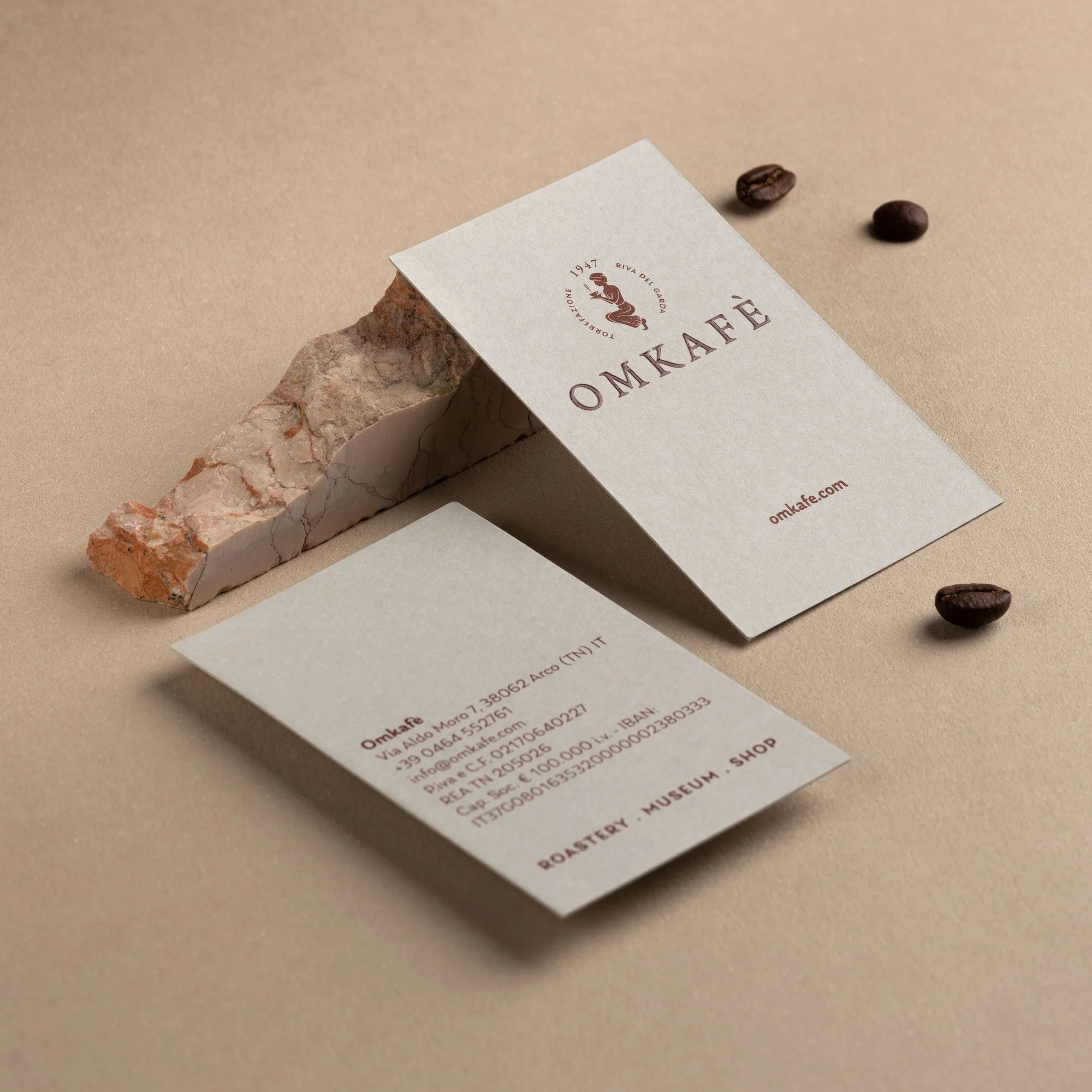 Una scheda di raccolta punti con un logo di una donna e una scatola di marmo su una superficie di colore beige, e due chicchi di caffè marroni nelle vicinanze.