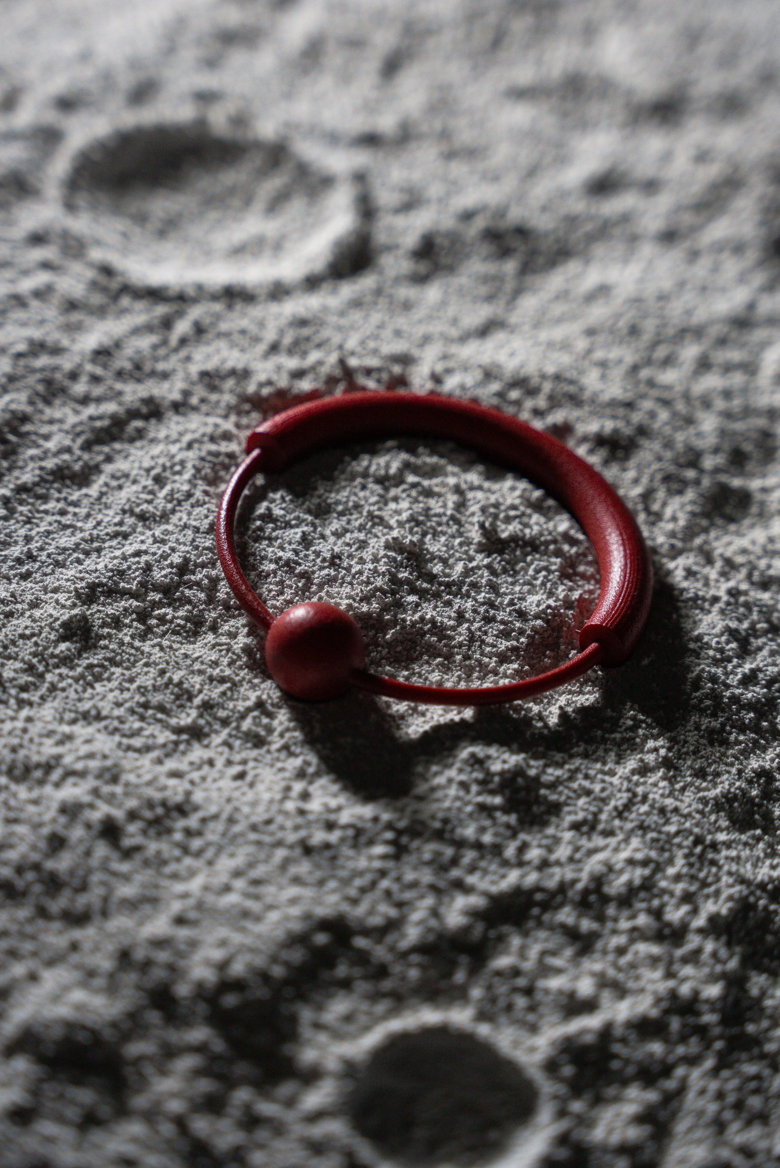 Un cerchio rosso con due palline sulla sabbia, creando ombre sul terreno.