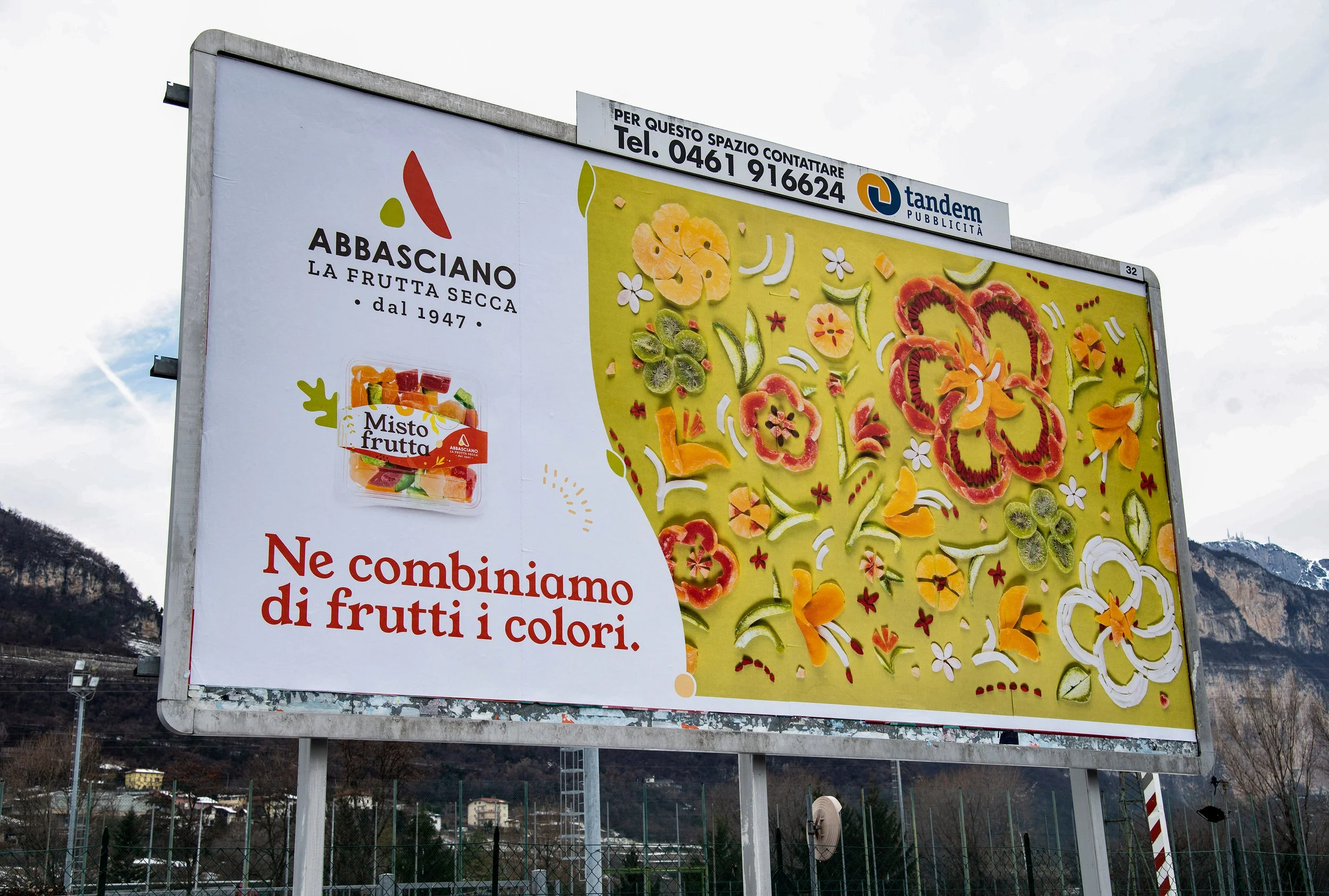 Un cartellone pubblicitario con immagini di frutta secca e fresca, e il logo di Abbasciano. Include informazioni di contatto e promuove una promozione sulla combinazione di frutti di diversi colori.