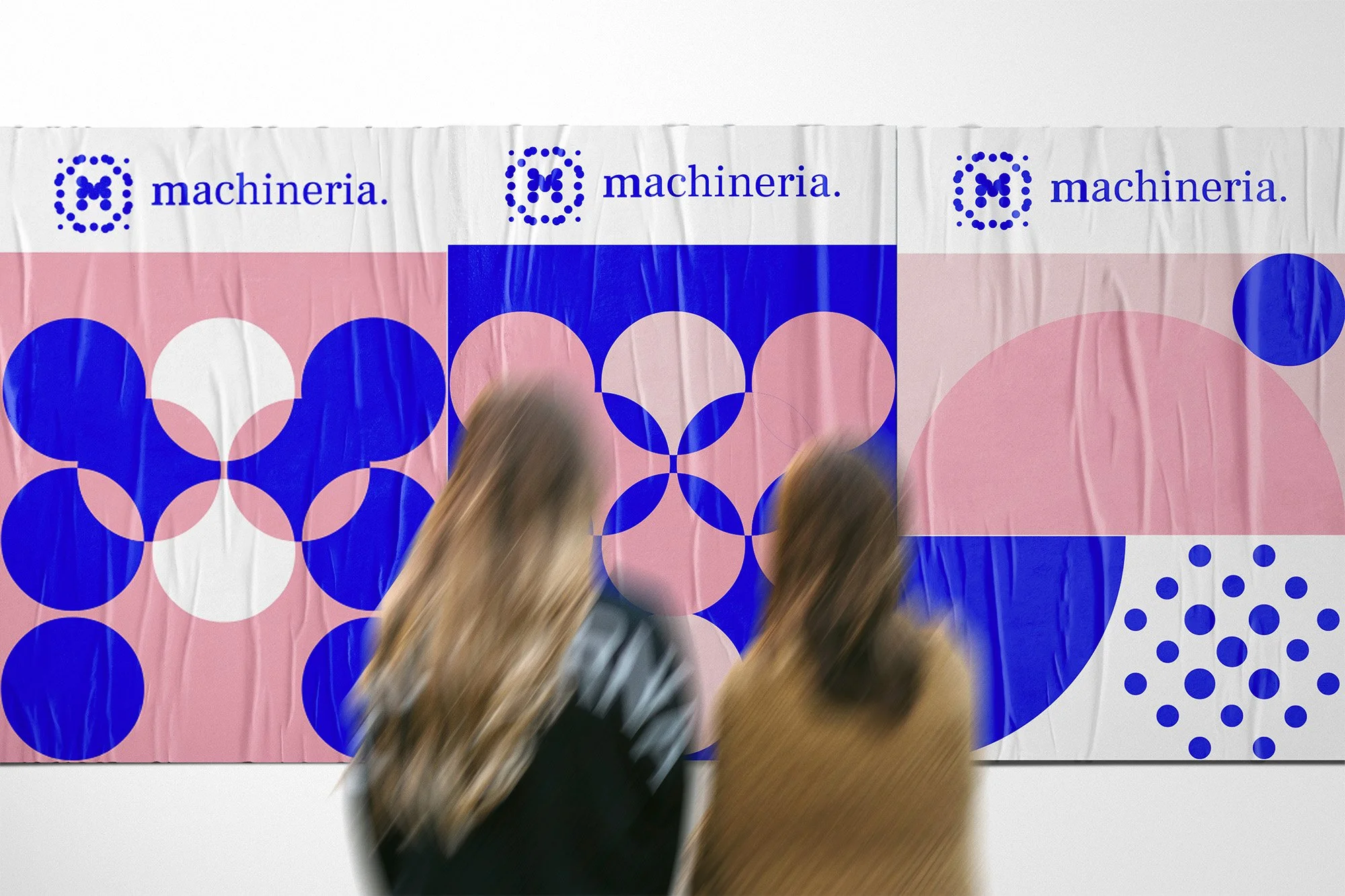 Una persona con cappotto nero osserva un pannello decorativo con cerchi di diversi colori. La parete ha la scritta 'macchina' con un logo di cerchi blu.