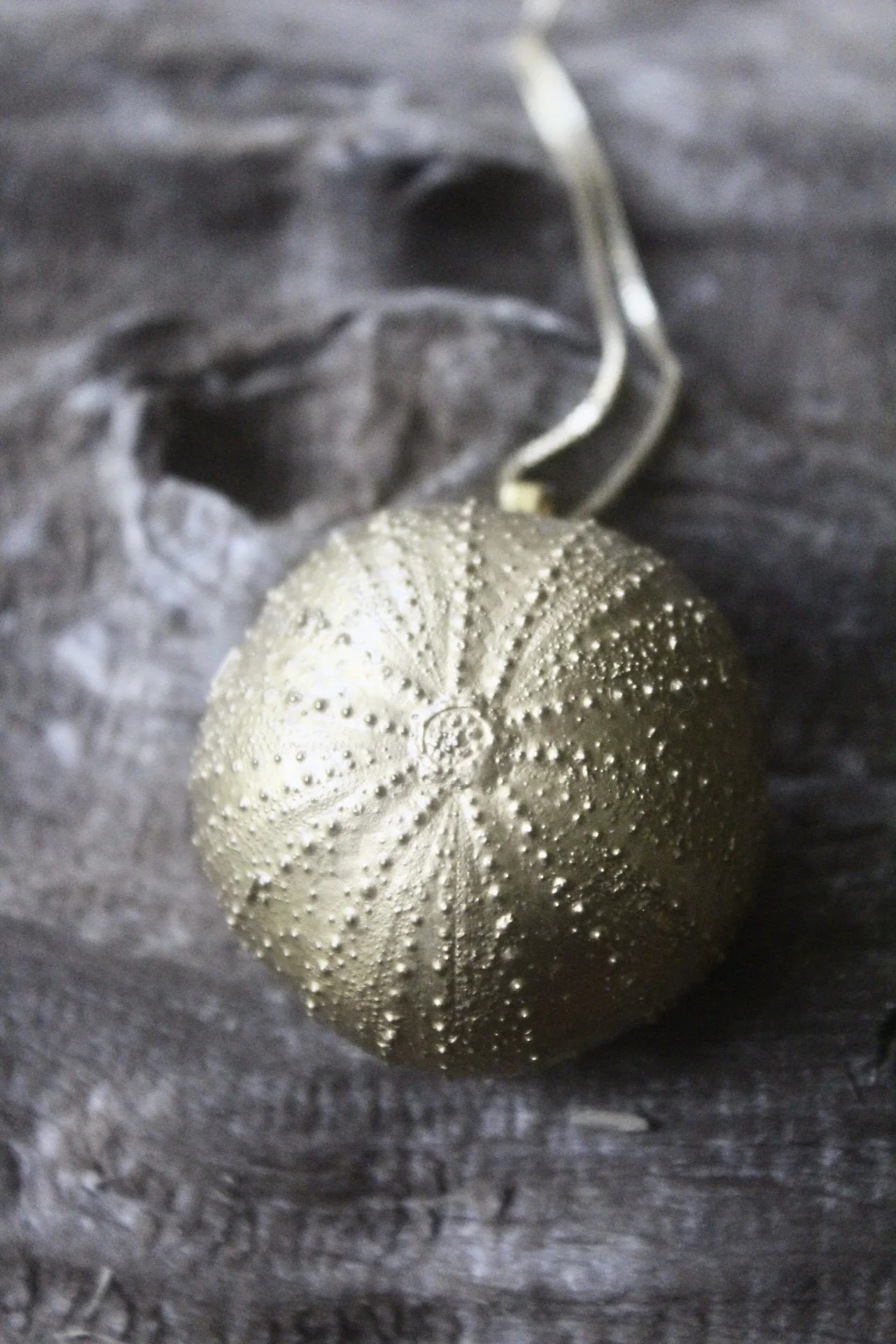 Close-up of a vintage Christmas ornament with intricate raised patterns, hanging on a dark, textured background.