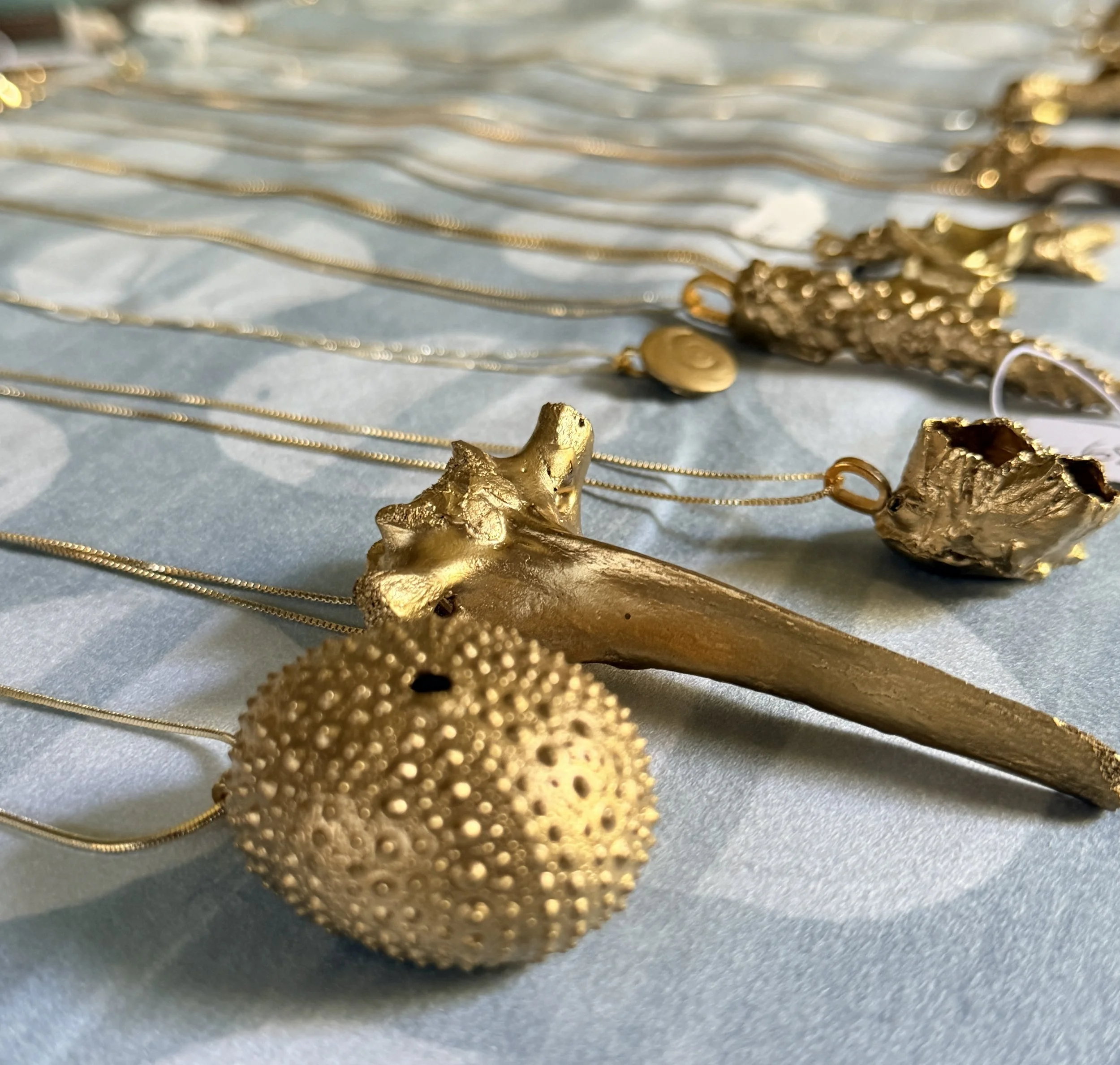 Close-up of various gold jewelry pieces, including necklaces and rings, laid out on a light blue surface.