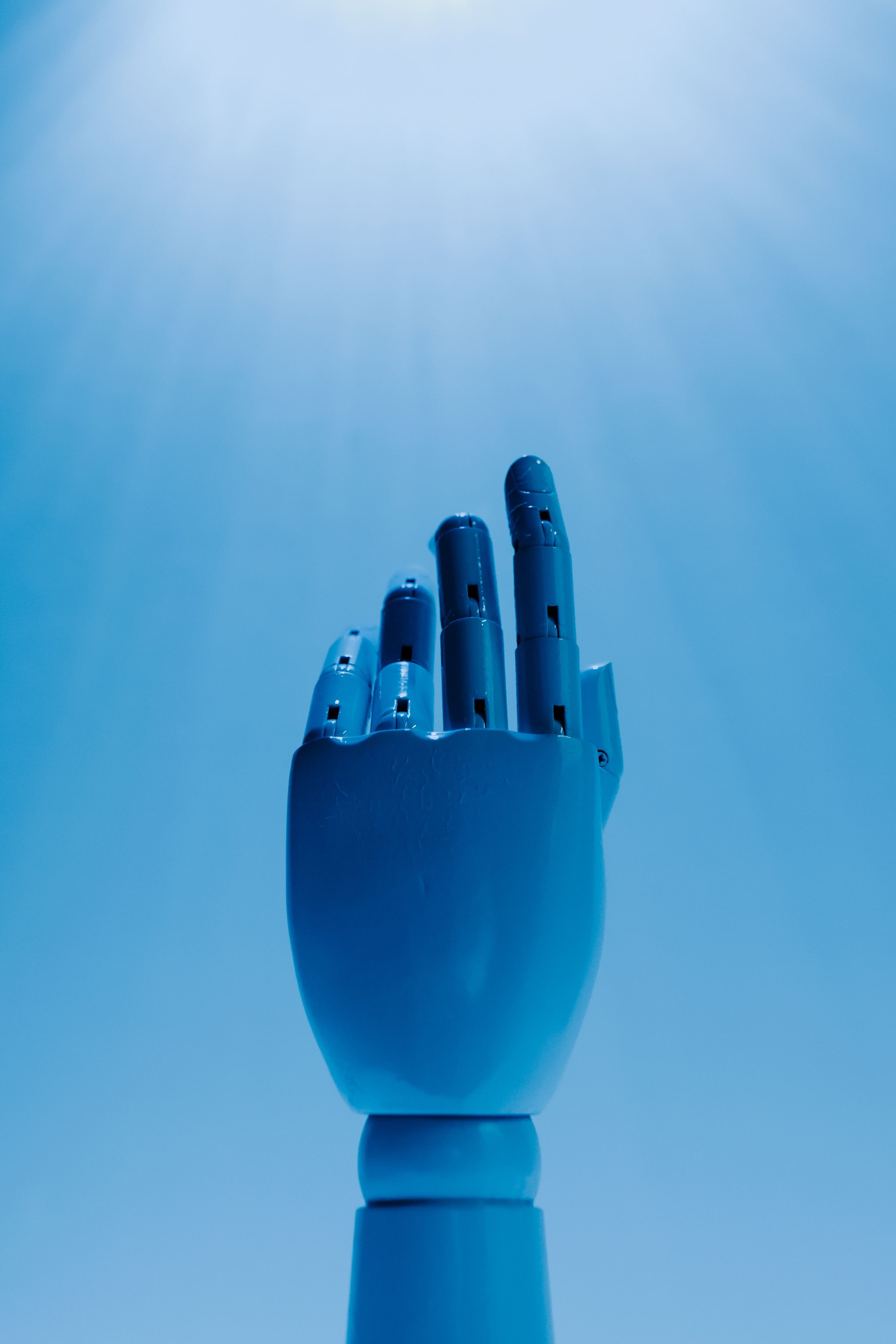 A white robotic hand reaching upward towards a blue sky with wispy clouds.