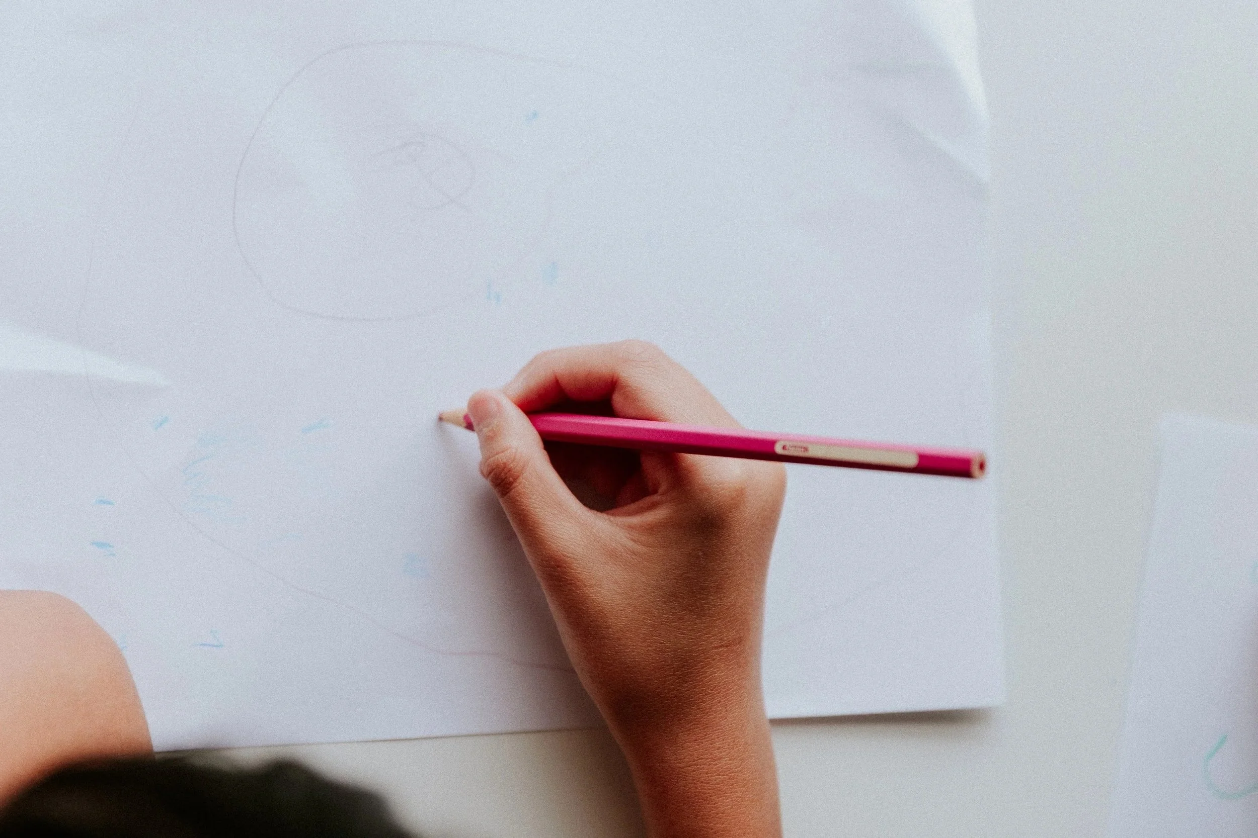 Person holding a pink colored pencil and drawing on a white sheet of paper.