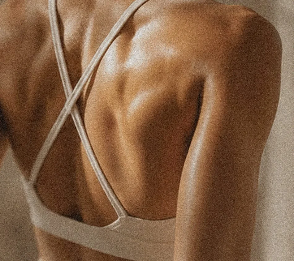 Close-up of a person wearing a beige or skin-colored strappy top, showing their shoulder and part of their back.