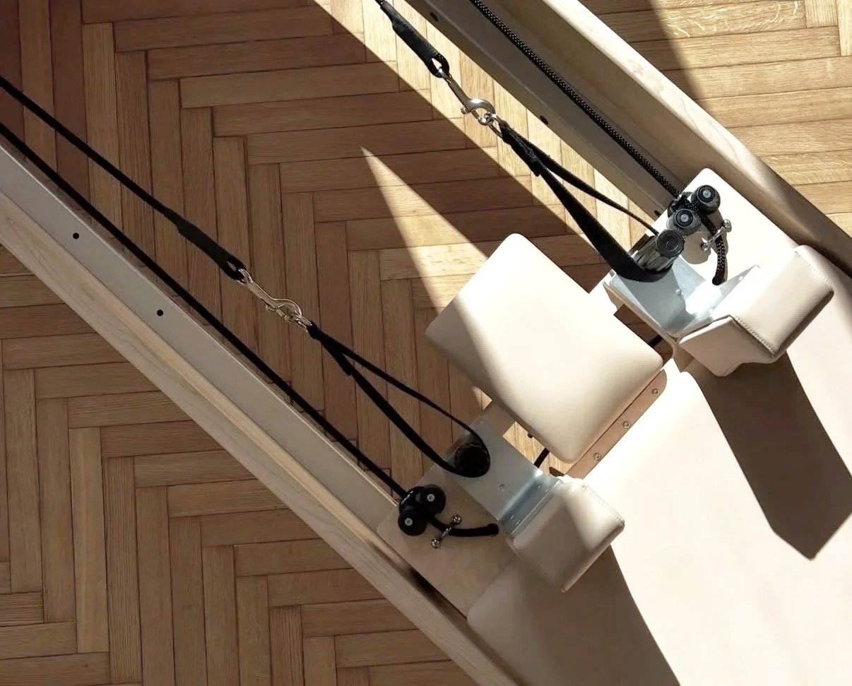 Image showing two chairs connected to a pulley system with ropes and pulleys, set up against a wooden floor and wall, with sunlight casting shadows.