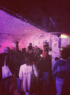 Folla di persone che ascolta una band dal vivo in un locale con decorazioni luminose sul soffitto. Casa delle Stelle, ambiente e associazione queer a Brescia