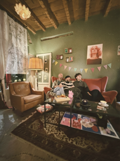 Una stanza accogliente con tre persone sedute sul divano, decorazioni colorate e un lampadario, atmosfera calda e casalinga. Casa delle Stelle, ambiente e associazione queer a Brescia