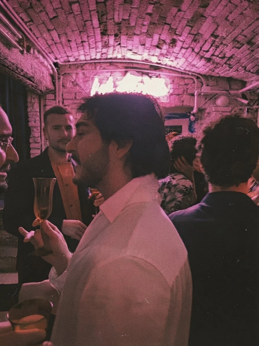 Un gruppo di persone che socializzano in un locale con pareti di mattoni e neon rosa. Casa delle Stelle, ambiente e associazione queer a Brescia