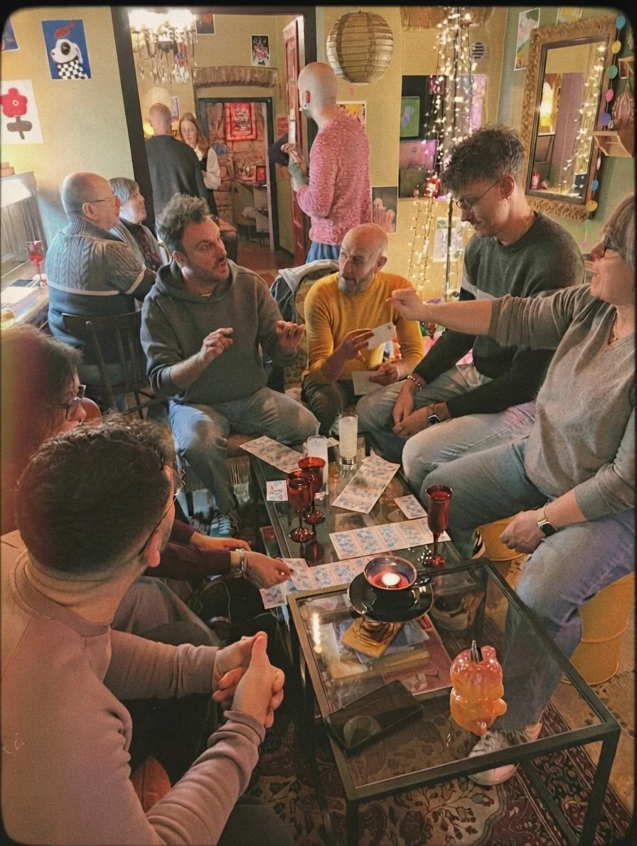 Gruppo di persone che giocano a tombola in una sala decorata con luci natalizie e pareti colorate. Casa delle Stelle, ambiente e associazione queer a Brescia