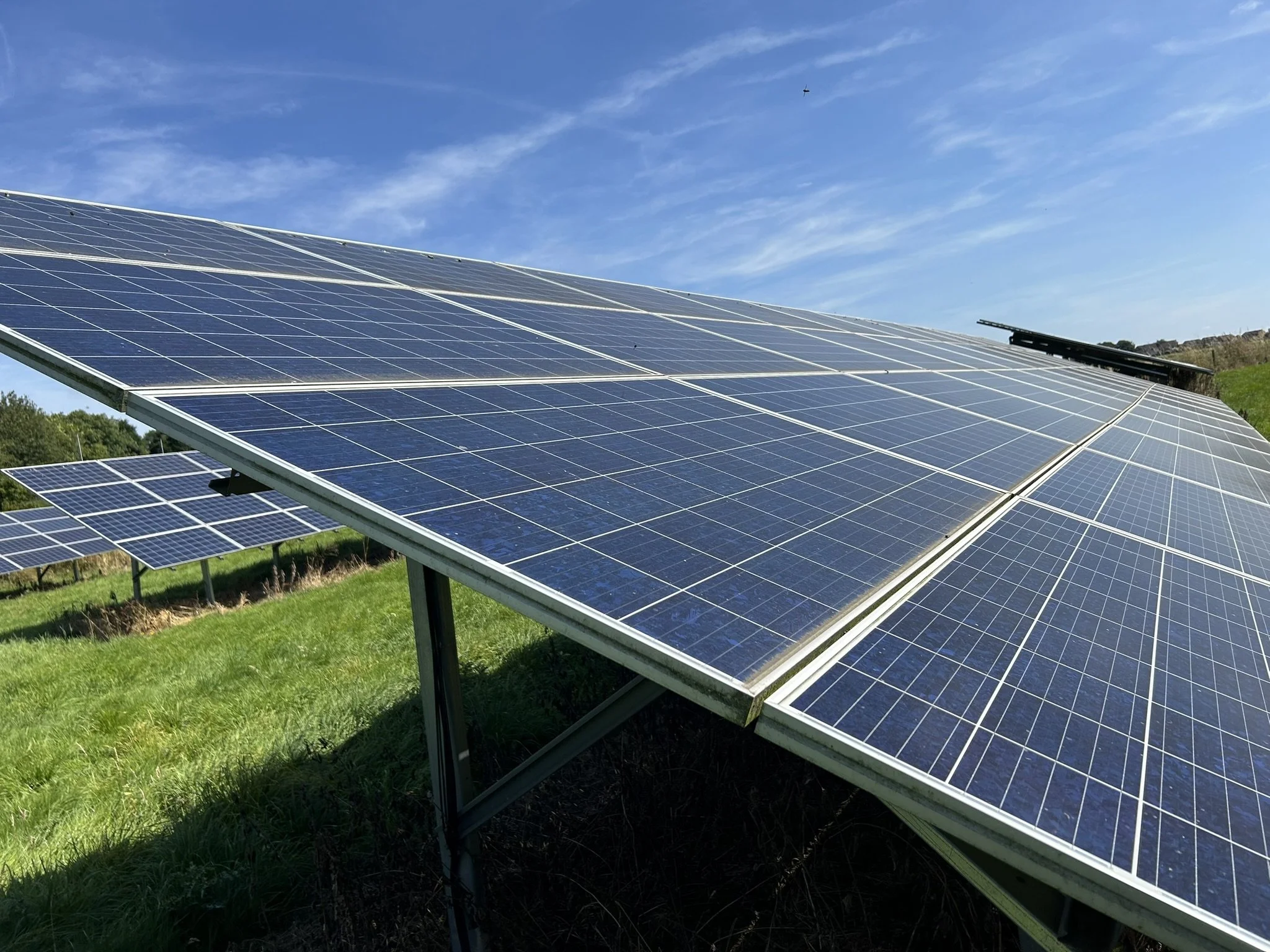 Multiple solar panels installed on a grassy field under a blue sky with a few clouds.