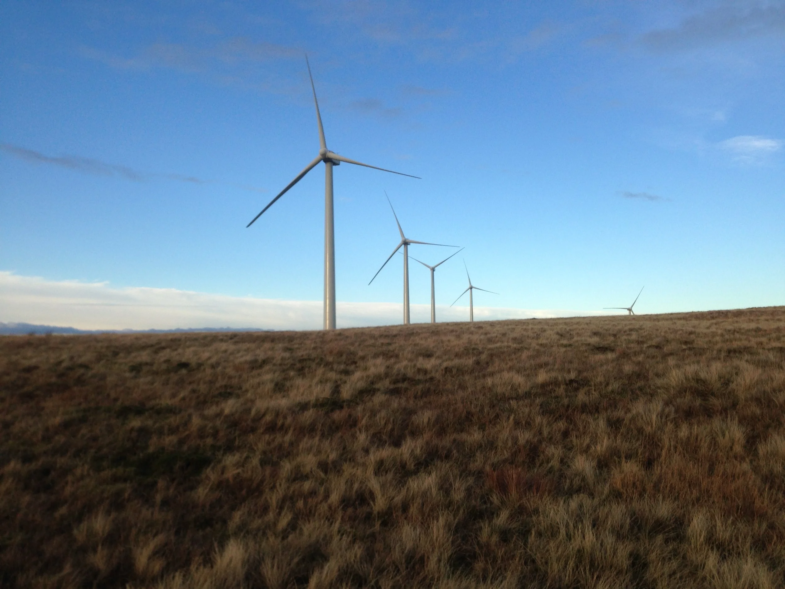 A row of wind turbines on a grassy hillside under a partly cloudy sky.