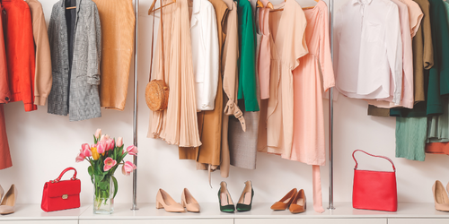 Clothing rack with various dresses, tops, and jackets, two red handbags, a glass vase with pink tulips, and three pairs of high heels.