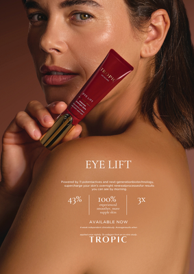 A woman with dark hair holding a red tube of eye lift cream close to her face and shoulder.