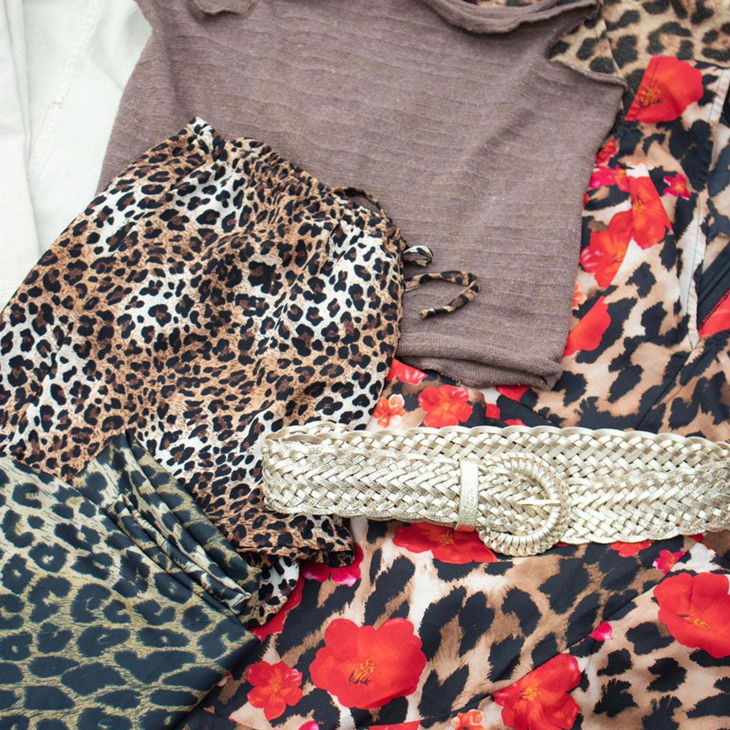 A variety of clothing items with animal and floral prints, including a leopard-print dress, a floral dress, and a basket-style bag on a flat surface.