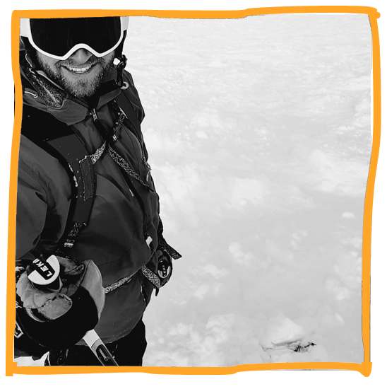 A person dressed in winter gear on snow, holding an ice axe, wearing sunglasses, smiling, with an orange border around the photo.