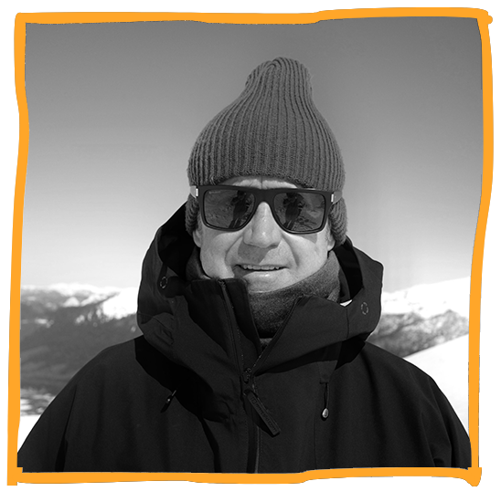 Man wearing a knit beanie, sunglasses, and winter jacket outdoors in snowy mountains.