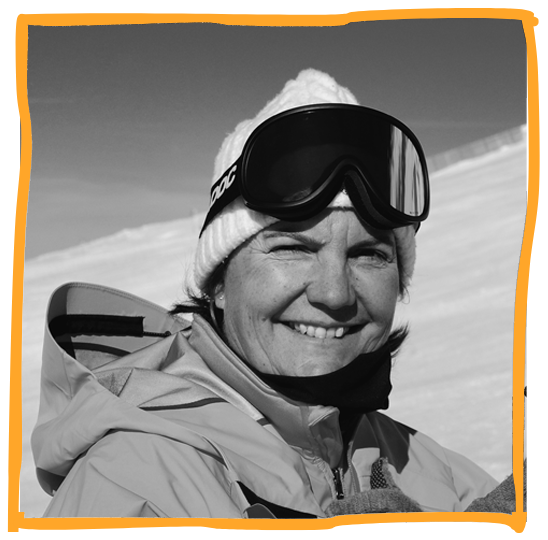 Smiling woman in winter gear, wearing ski goggles, beanie, and a ski jacket, in a snowy mountain setting.