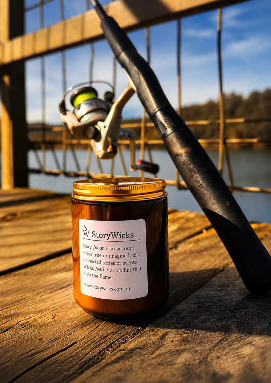A fishing rod and reel leaning against a wooden railing on a dock, with a jar labeled "StoryWicks" in the foreground, outdoors near a body of water under a clear sky.