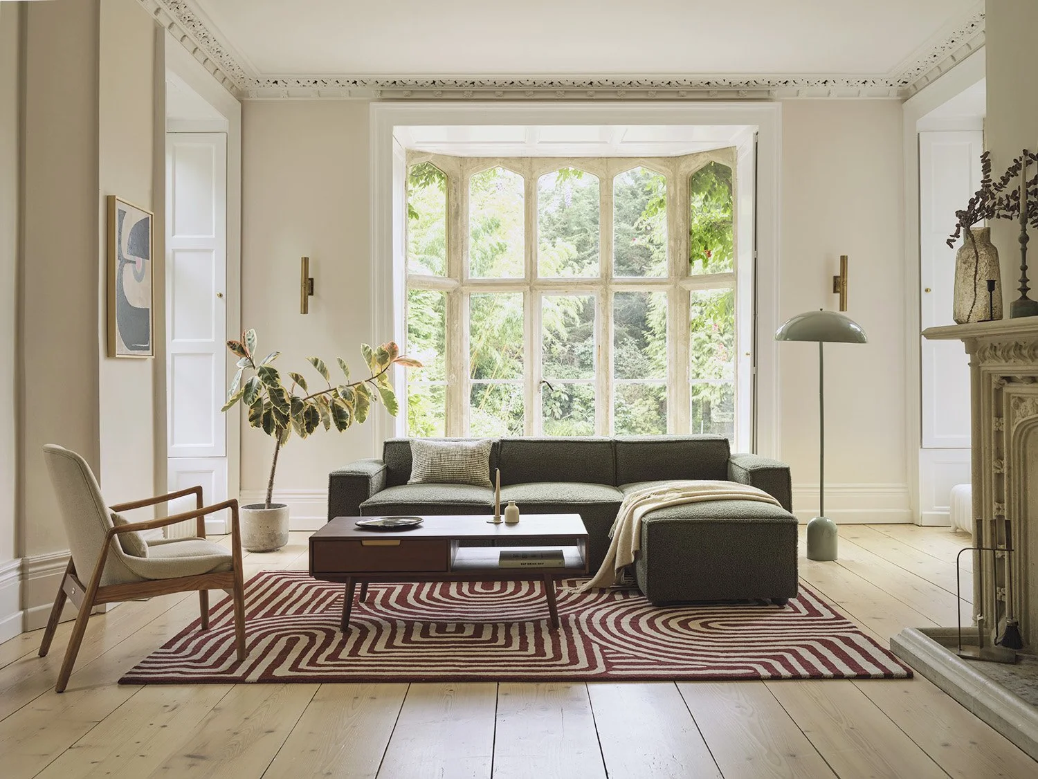 Living room with large window, gray sofa, armchair, red and white patterned rug, coffee table, floor lamp, and decorative items.