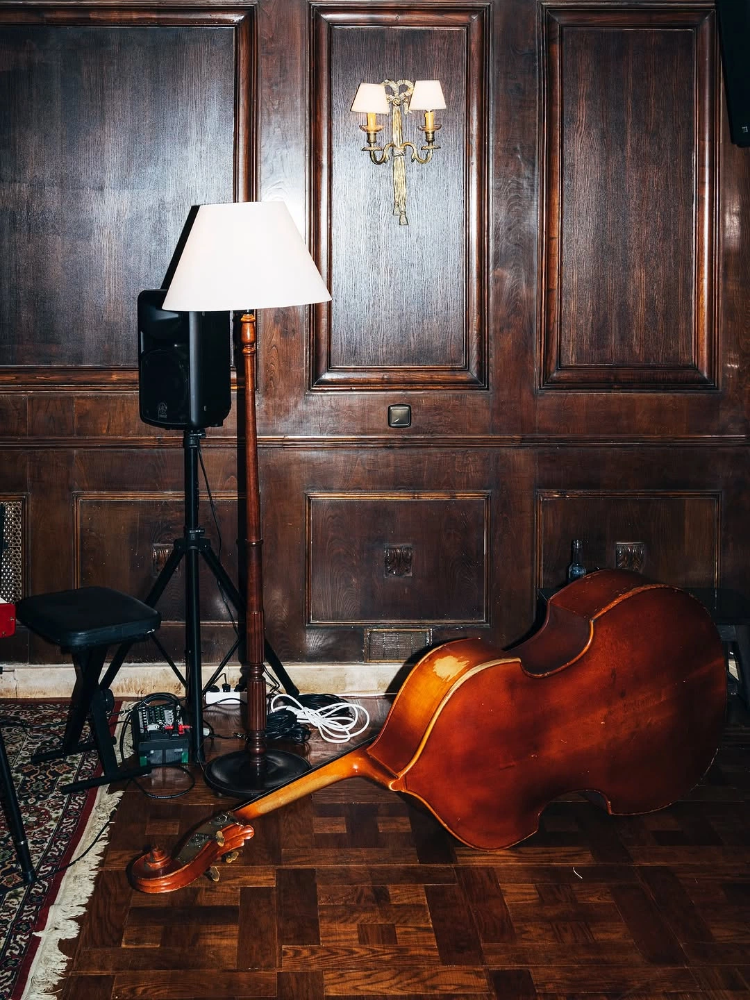 Double bass resting in a wood-panelled room beside performance equipment.
