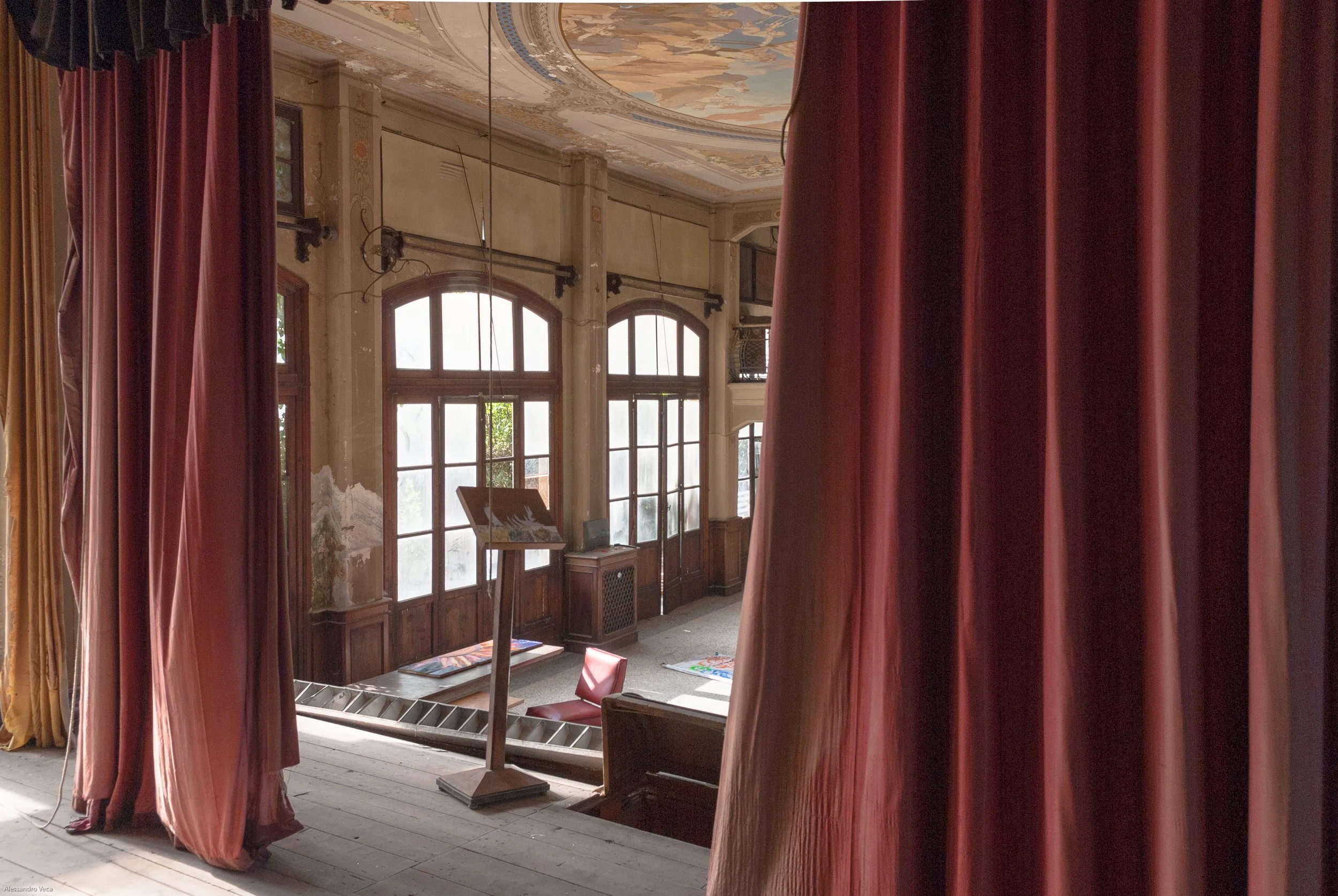 Interno del Teatro Marinoni tra sipari rossi, arredi e luce naturale proveniente dalle finestre