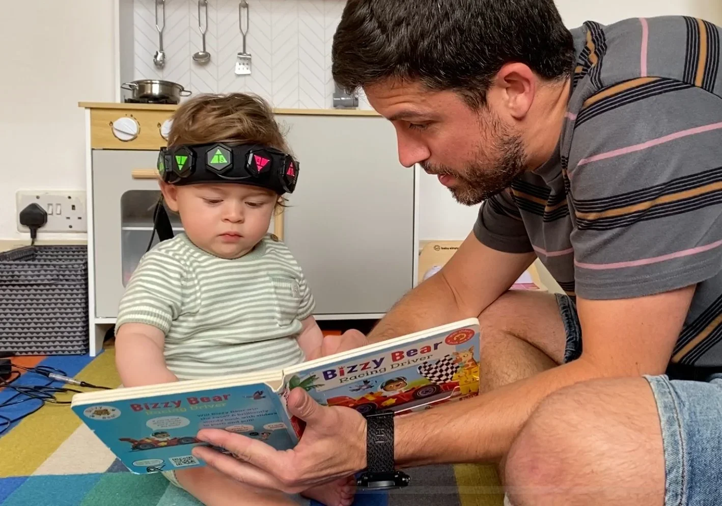 Infant wearing the Gowerlabs LUMO fNIRS wearable brain imaging system during a naturalistic developmental neuroscience research session while interacting with a researcher.