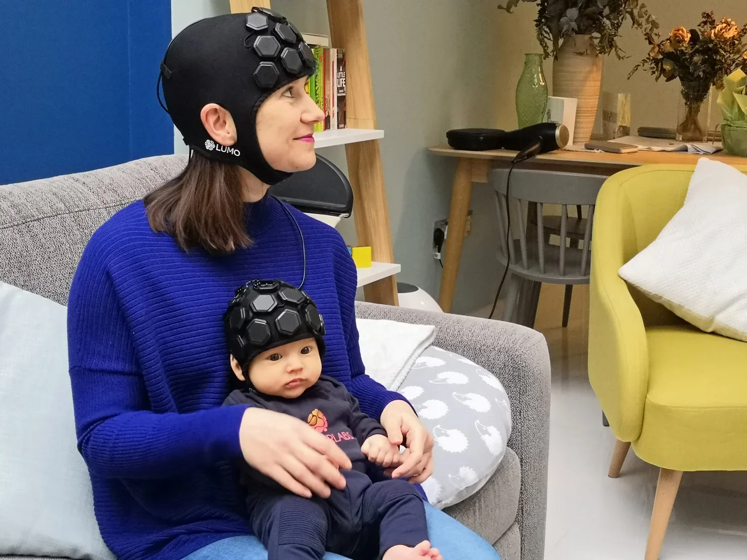 Adult and infant wearing the Gowerlabs LUMO fNIRS high-density wearable brain imaging system during a naturalistic neuroscience research session.
