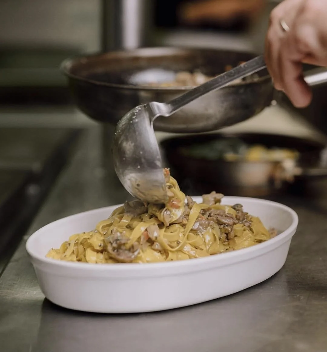 Una persona sta versando un piatto di pasta con funghi e sugo in una ciotola bianca.