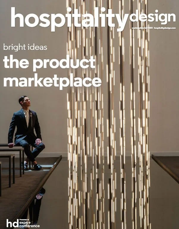 A conference poster titled 'hospitality design' with the subtitle 'bright ideas, the product marketplace.' The background shows a modern, illuminated vertical decorative element and a man in a suit sitting on a bench looking upwards.