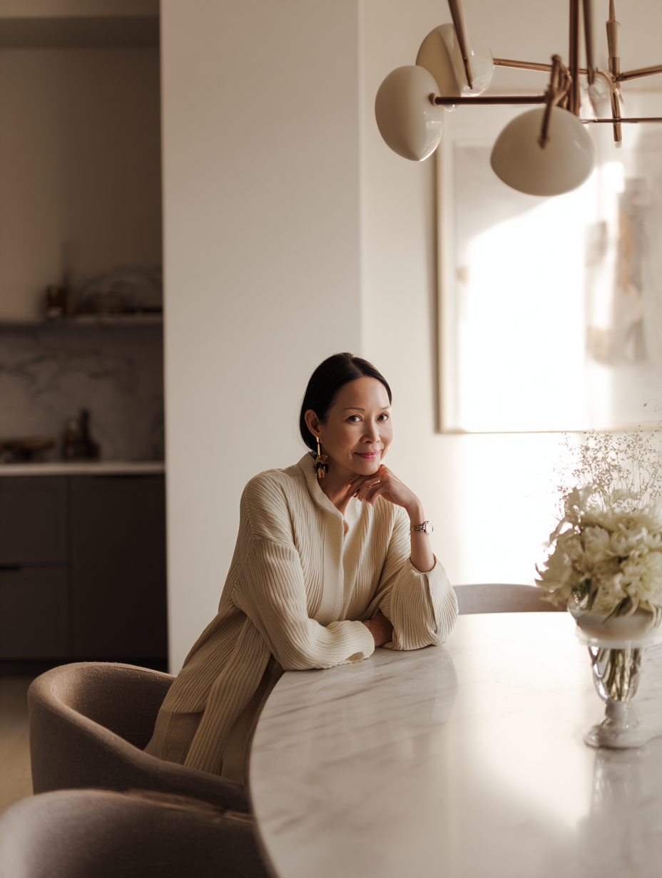 Premium Squarespace Template for Interior Designers. A woman sitting at a marble dining table with a floral arrangement, in a well-lit, modern kitchen or dining area.