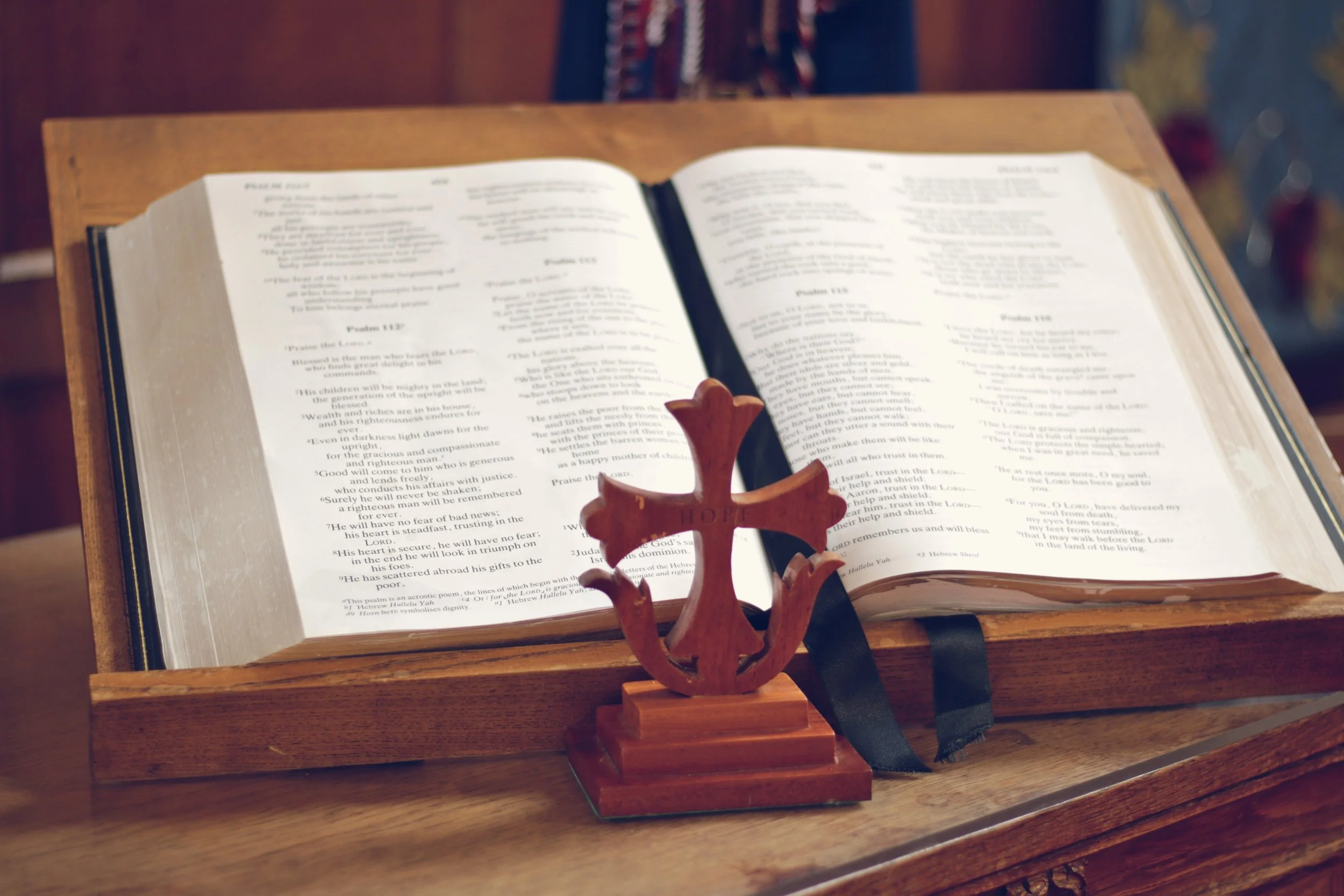 Open Bible placed on a wooden lectern with a decorative metal stand in front of it.