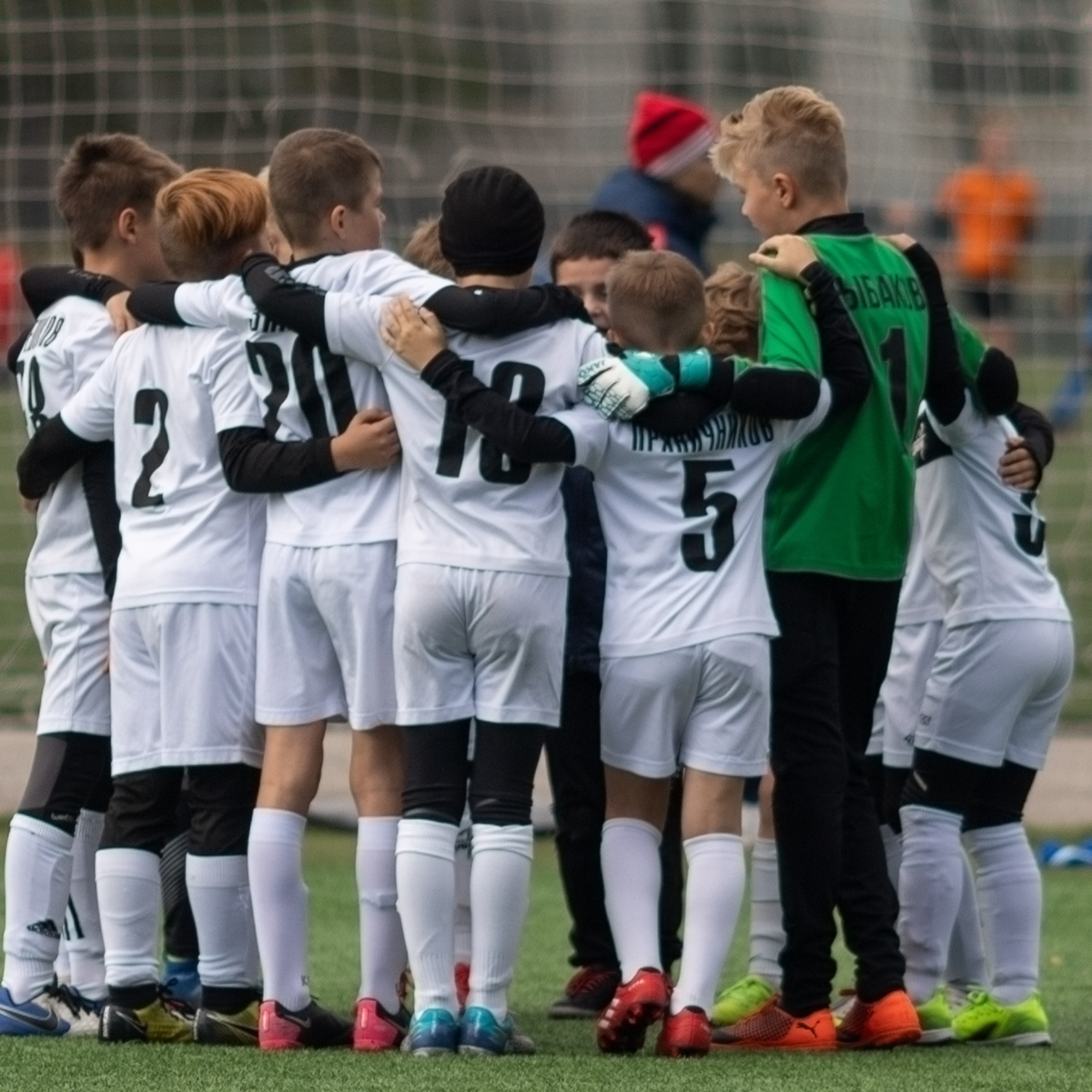 Youth football team huddled together in a group hug on the field before the game.