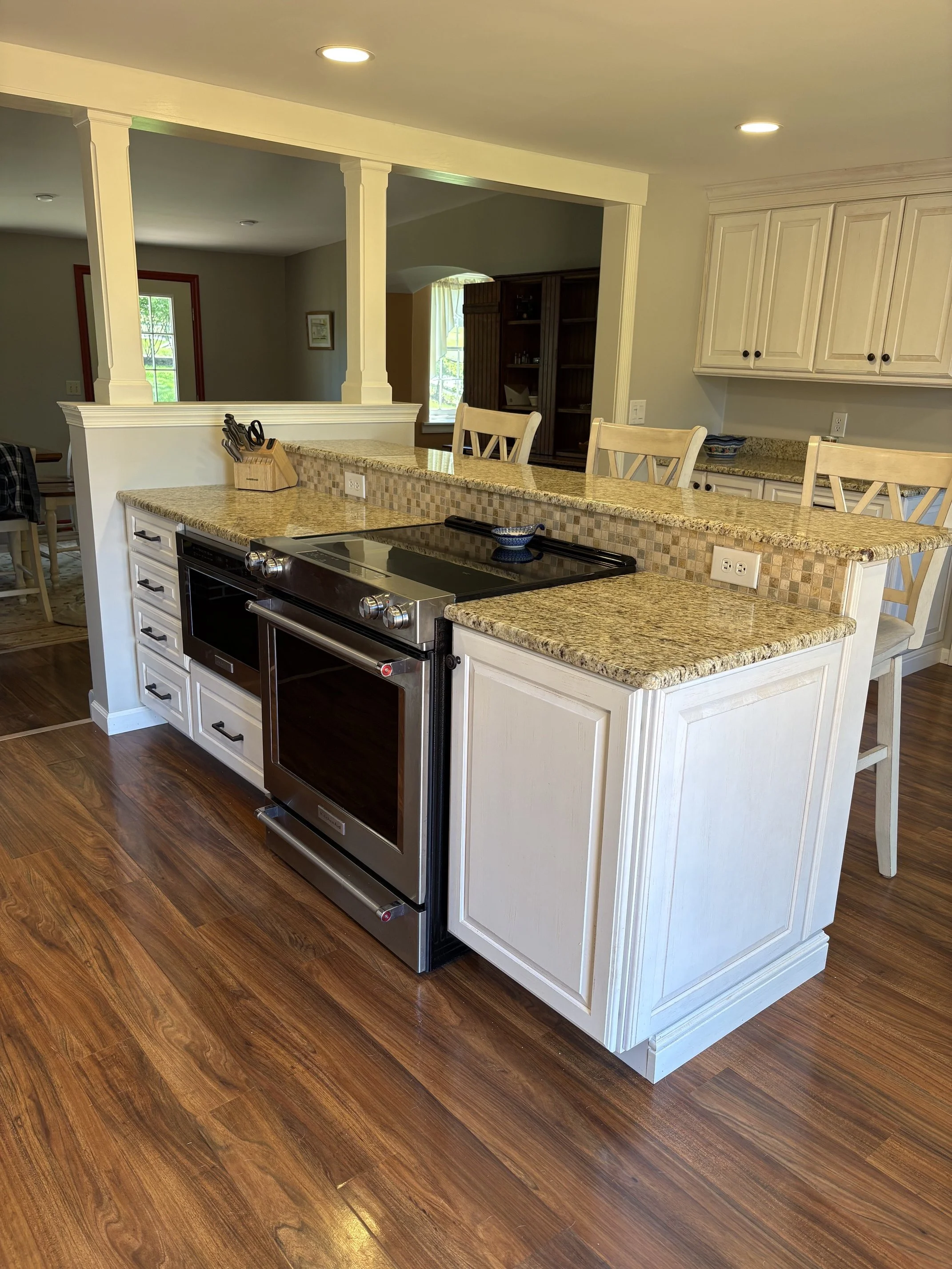 Modern kitchen with granite countertops, white cabinets, a black stove, and wooden flooring. Open layout with a breakfast bar and seating area.