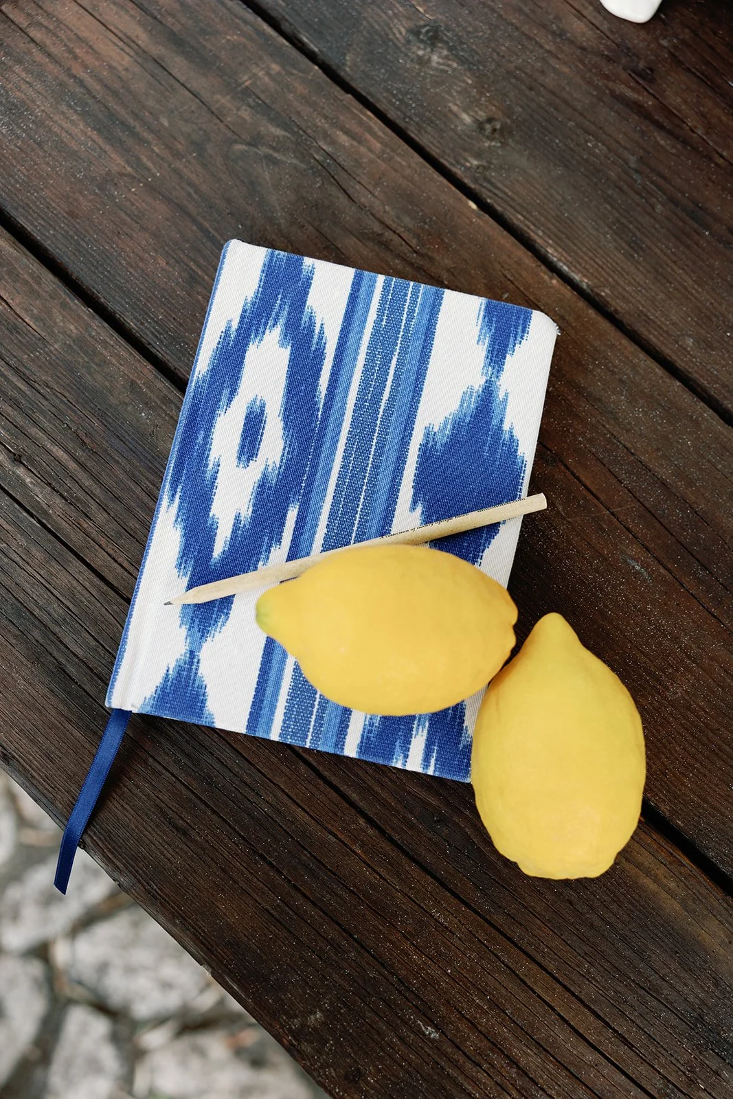 Zwei Zitronen, eine Zitronennadel und eine blaugemusterte Stoffserviette auf einem dunklen Holzoberfläche.