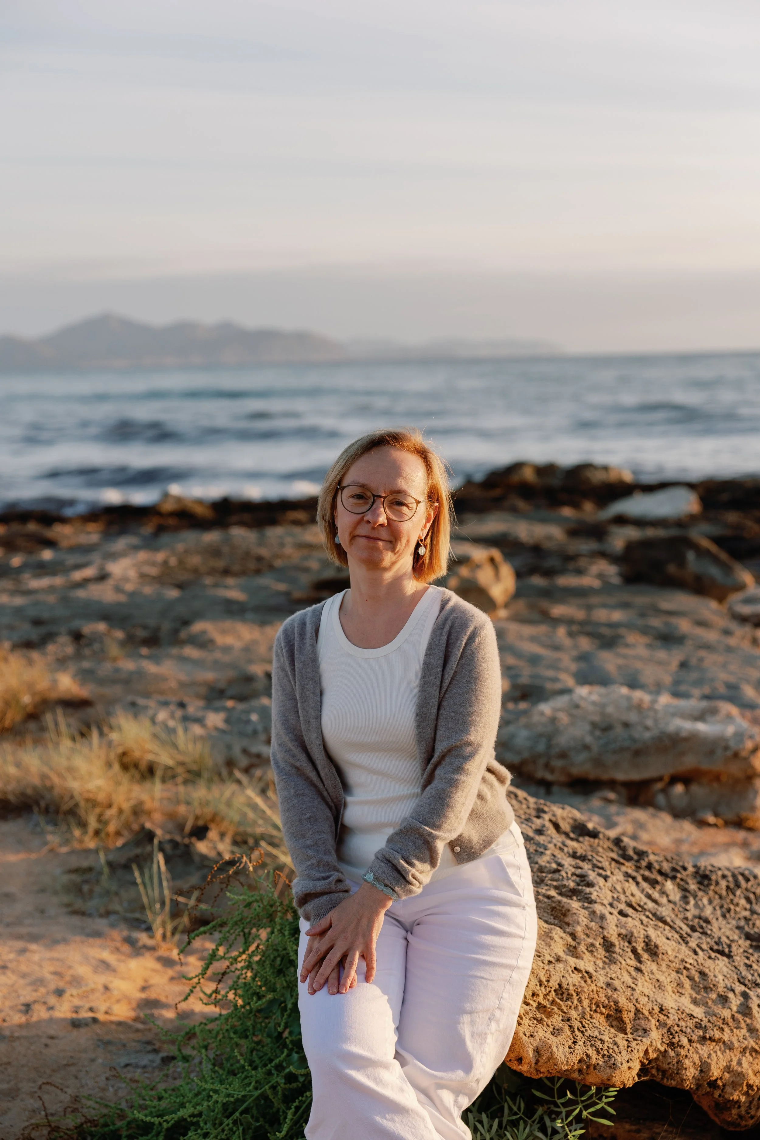 Dr. Doreen Kuschel sitzt am Strand vor dem Meer, während die Sonne untergeht.
