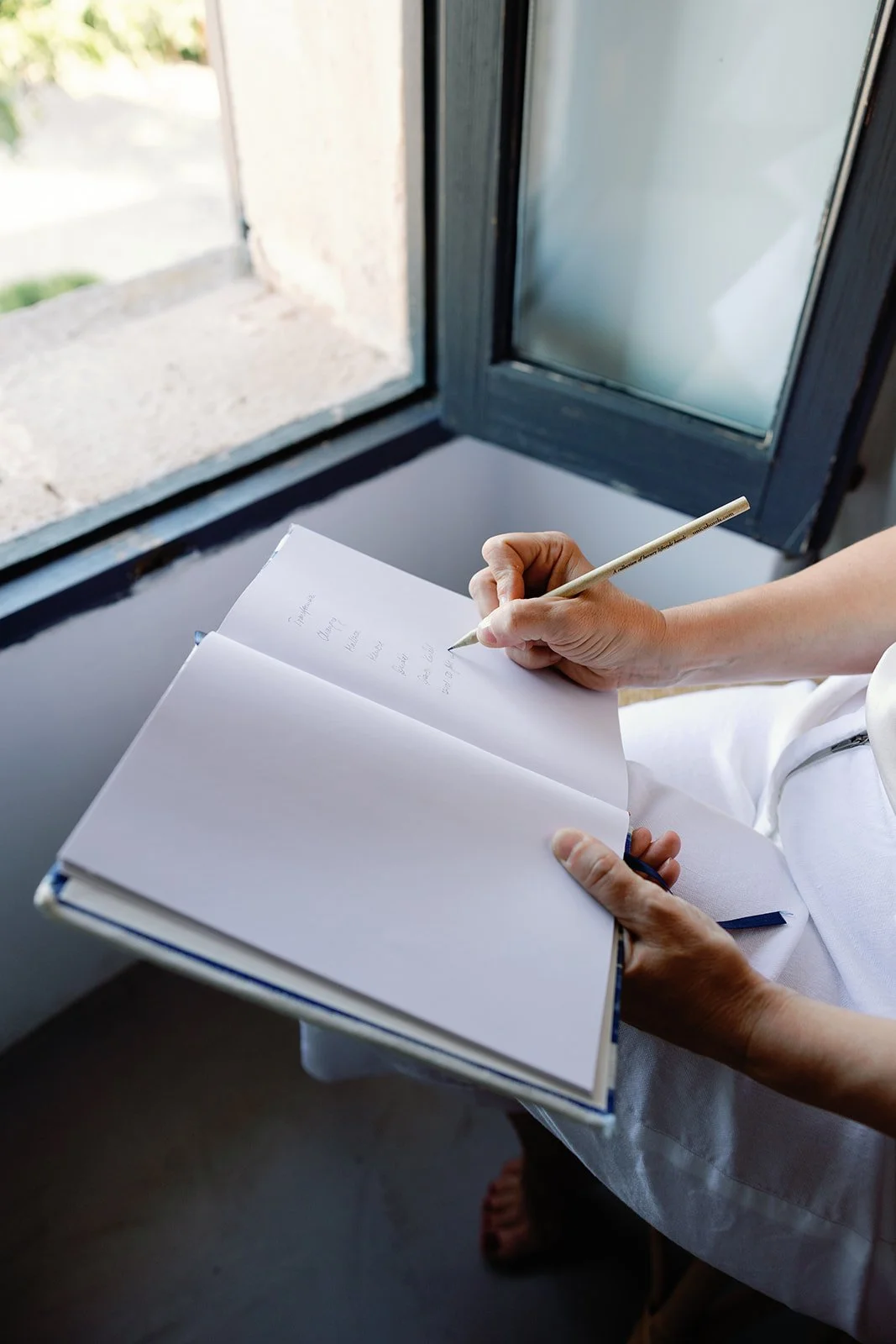 Person schreibt in ein offenes Buch an einem Fenster.