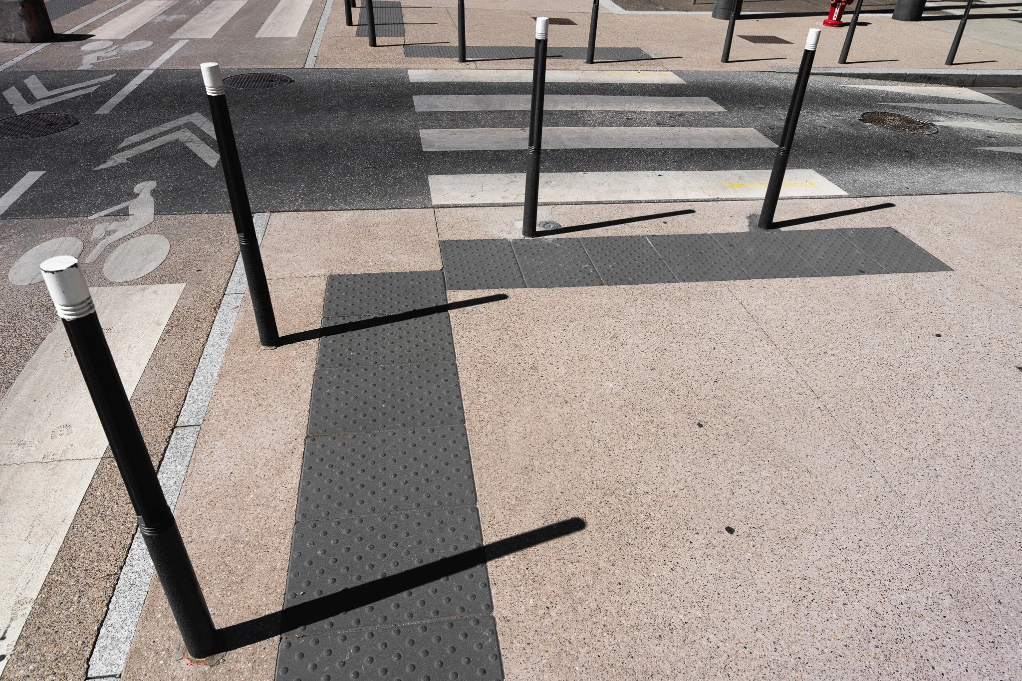 Passerelle piétonne avec des poteaux noirs et blancs, une piste cyclable, et des marquages au sol pour la circulation et la sécurité peinte sur la chaussée et le trottoir.