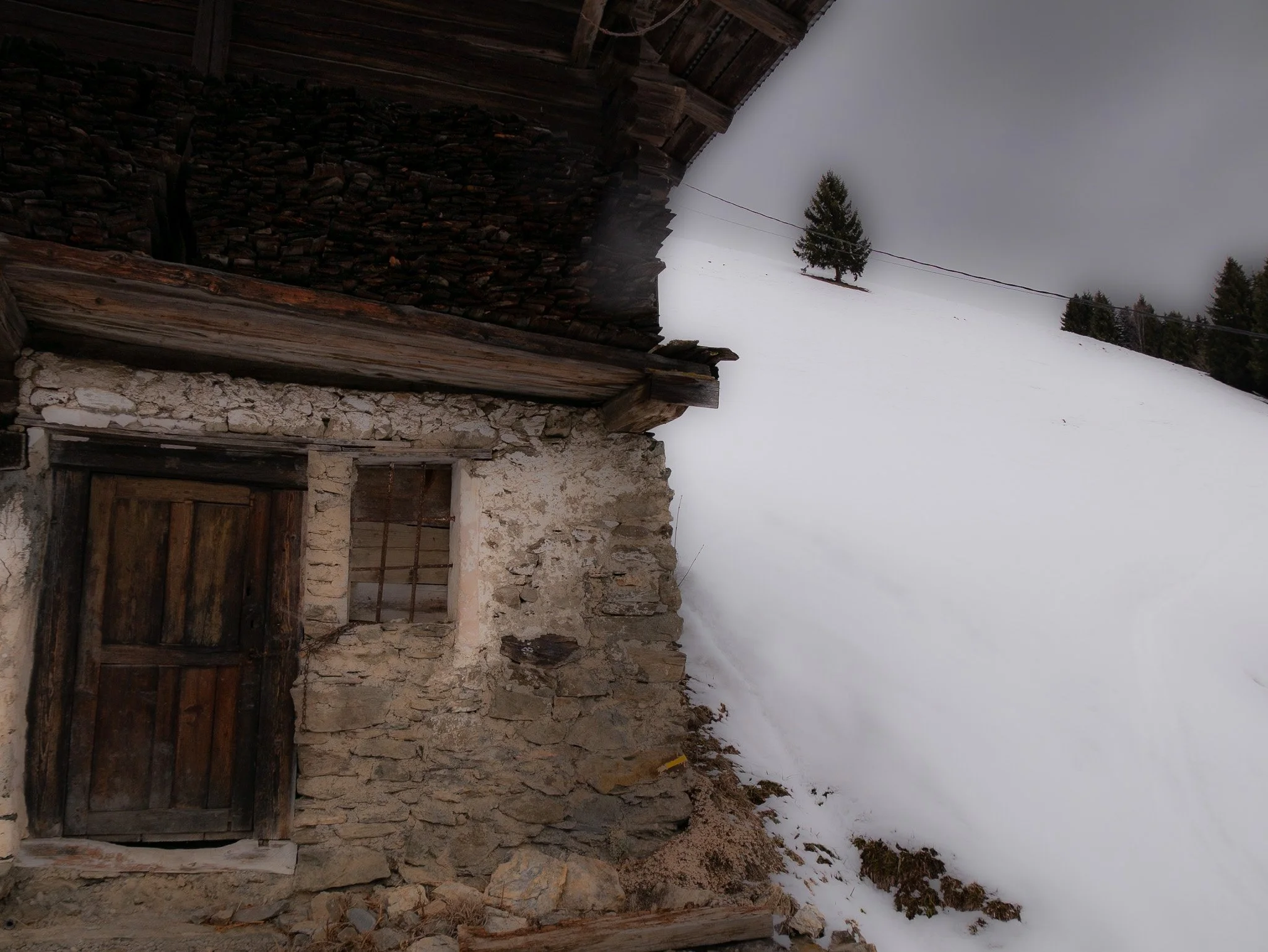 Une vieille maison en pierre et bois dans un paysage enneigé avec des arbres et un ciel nuageux.