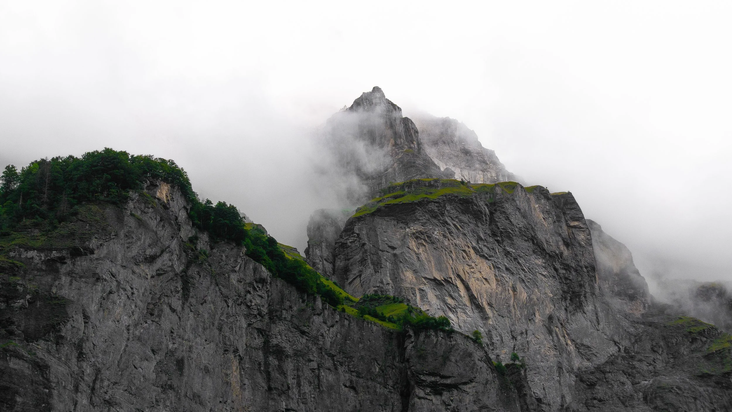 Montagne escarpée enveloppée de brouillard, avec des parties recouvertes de verdure.