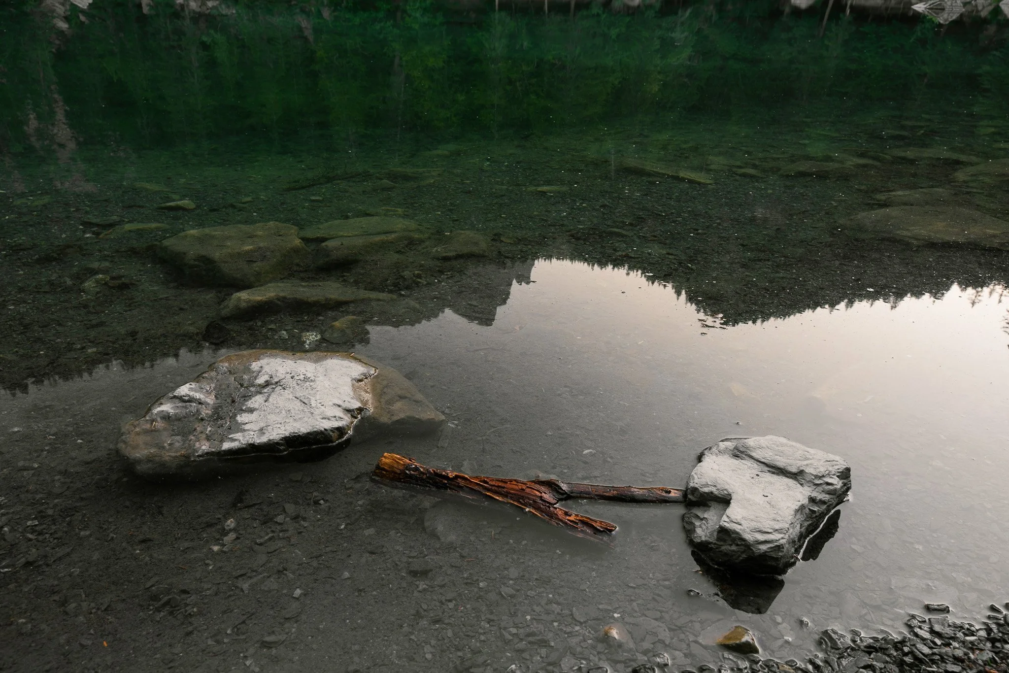 Un étang entouré d'arbres, avec des rochers au premier plan et la reflection des arbres dans l'eau calme.