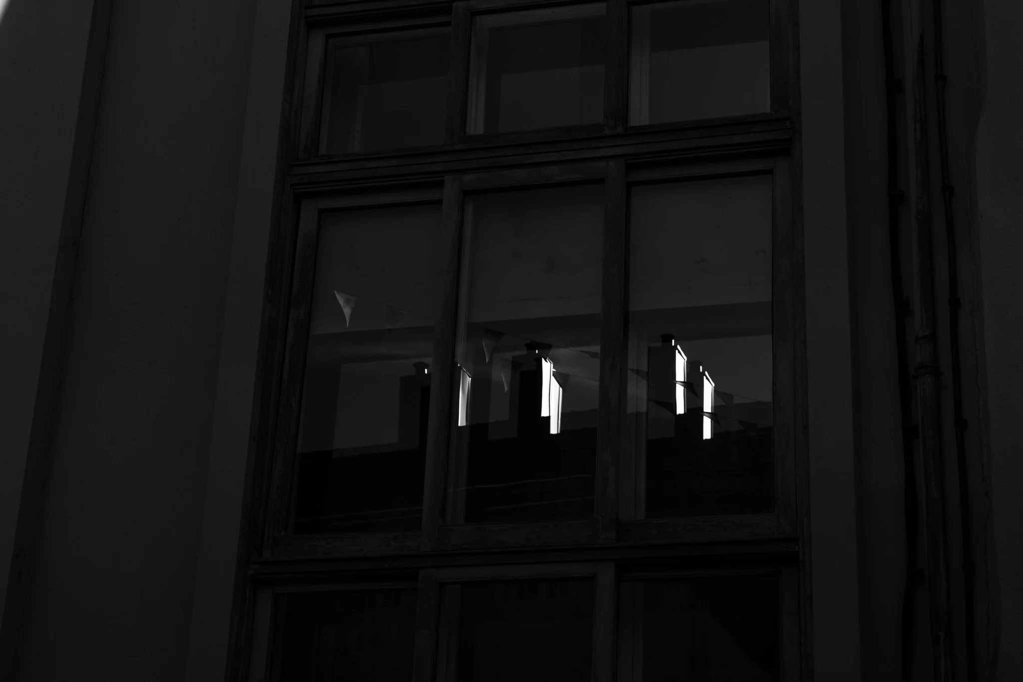 Fenêtre avec cadre en bois dans un mur gris, vue vers l'intérieur éclairé avec des lampes suspendues.
