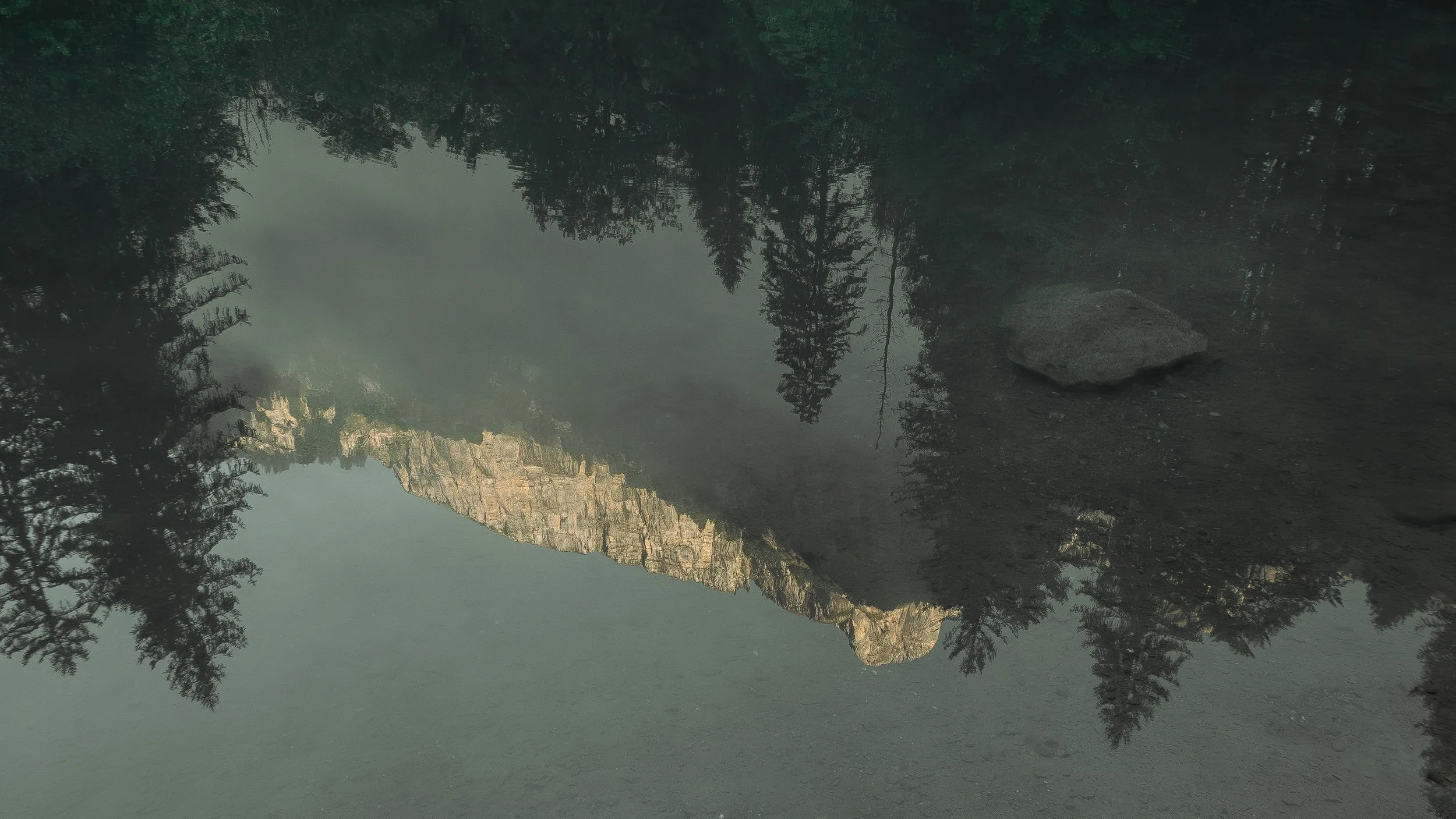 Reflet d'une montagne et d'arbres dans un lac ou une rivière calme.