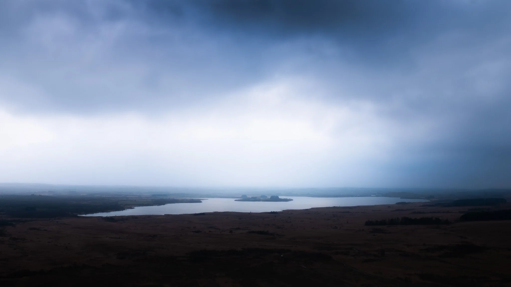 Ciel orageux avec des nuages sombres sur un paysage de plaines et un lac au loin