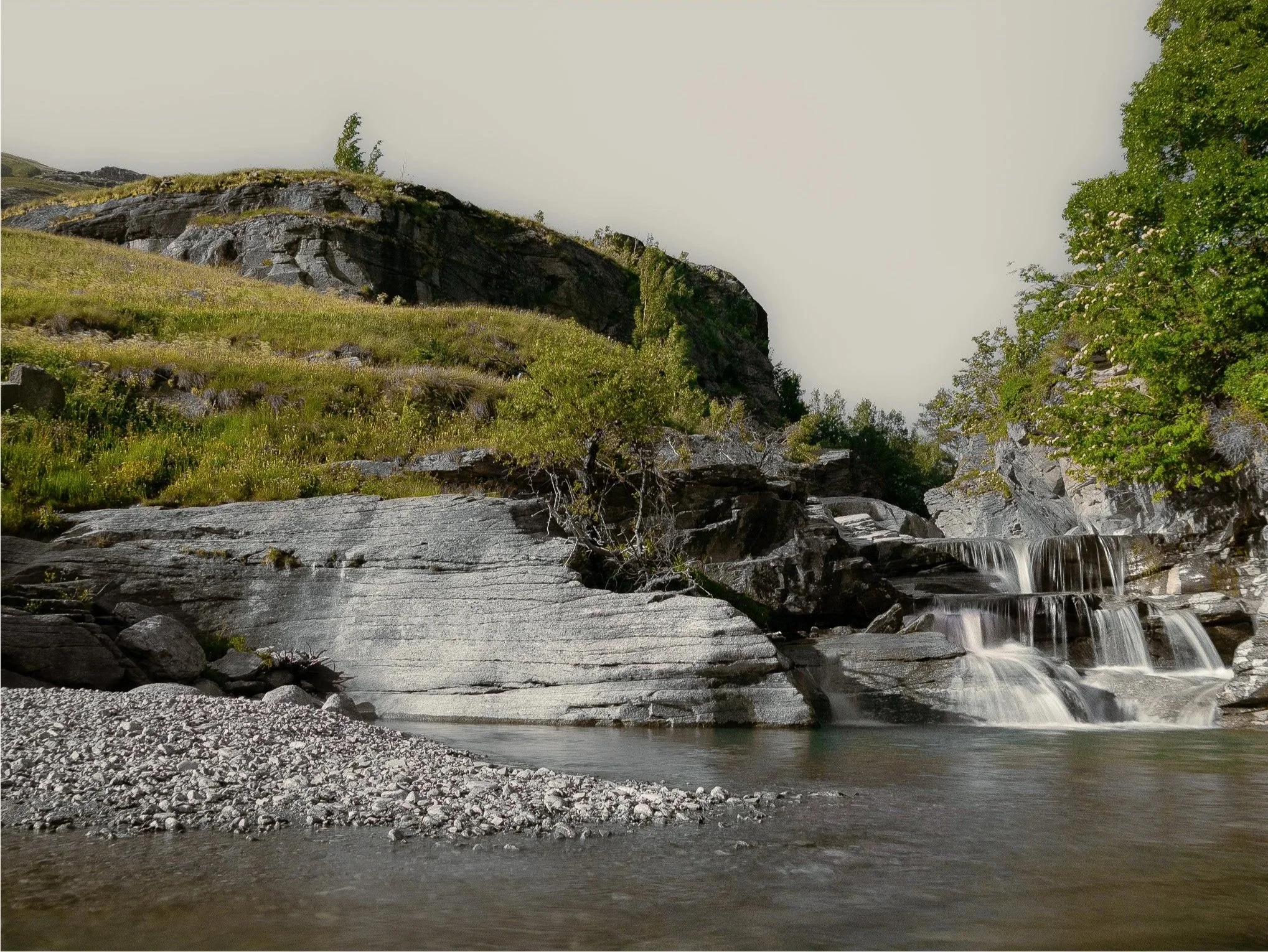 Une cascade d'eau coule le long de rochers dans une région montagneuse avec de la verdure et des arbres.