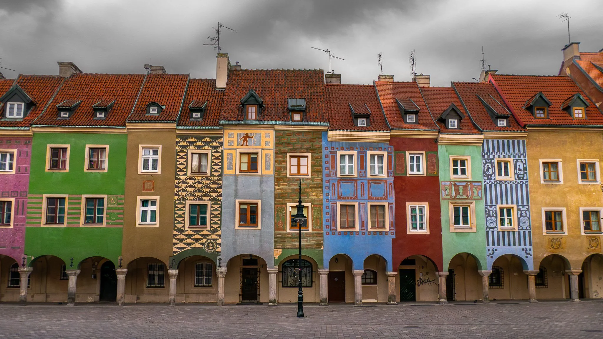 Haut d'un bâtiment coloré avec plusieurs facades peintes, tout au long d'une rangée, avec un ciel nuageux en arrière-plan.