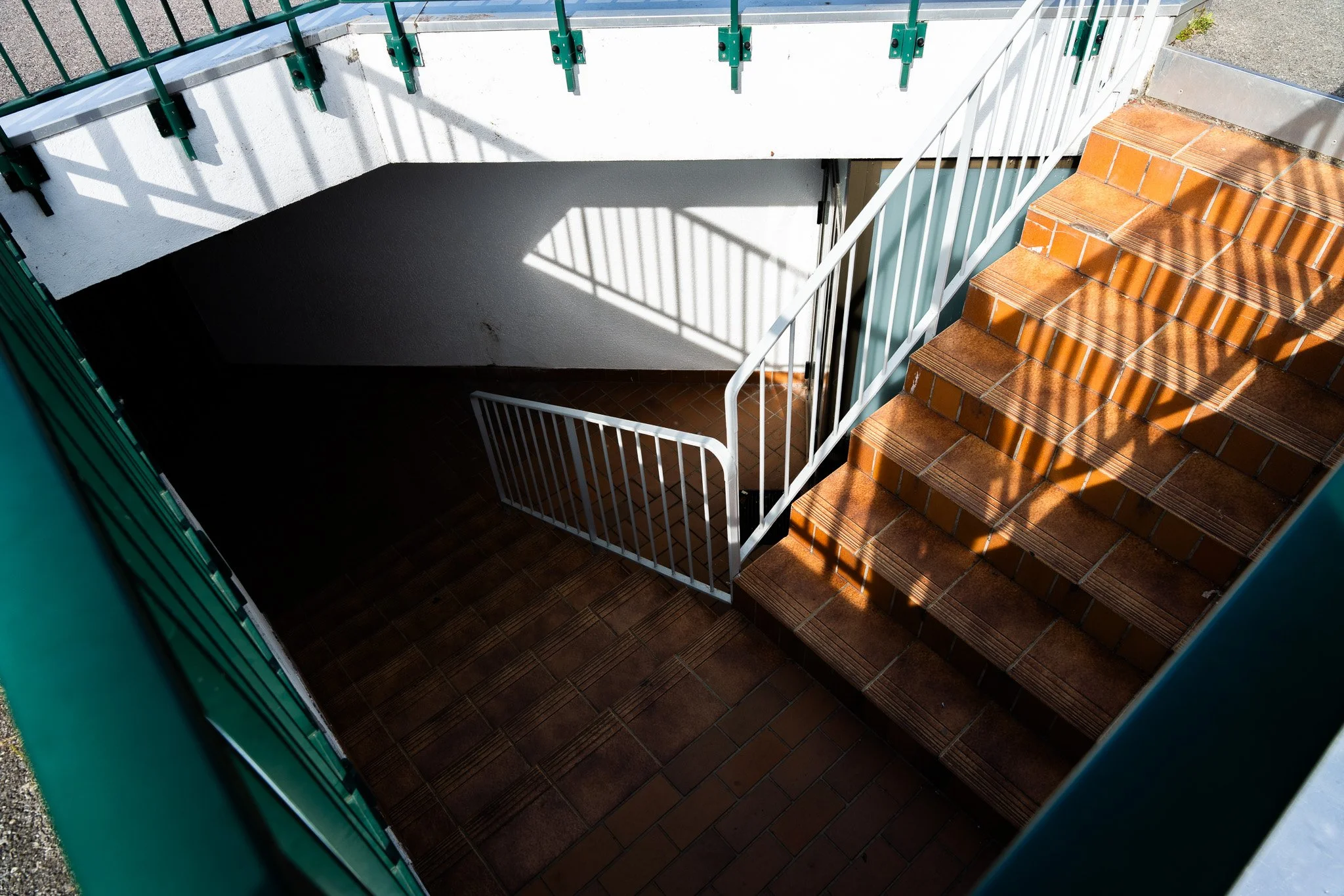 Escalier extérieur avec marches en tuile orange, rampe en métal blanc, et un espace en dessous avec murs blanc et noir.