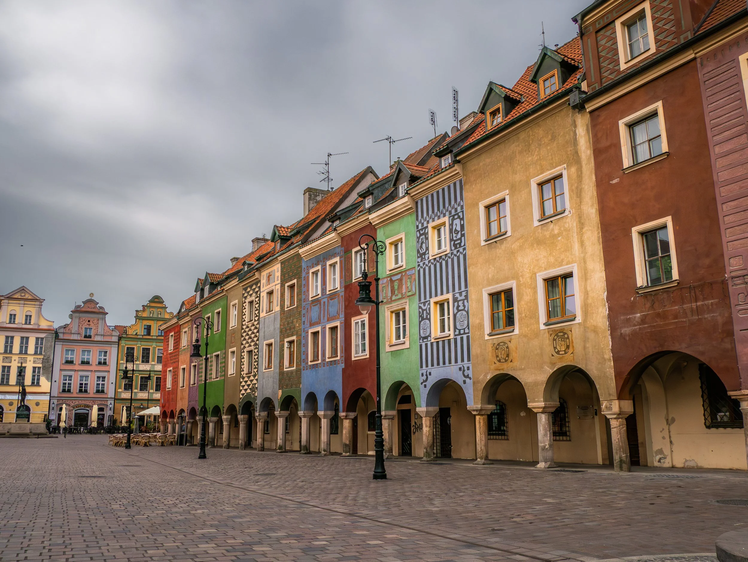 Une place pavée avec des bâtiments colorés de plusieurs étages, certains ornés de fresques ou motifs peints, et un lampadaire au premier plan.
