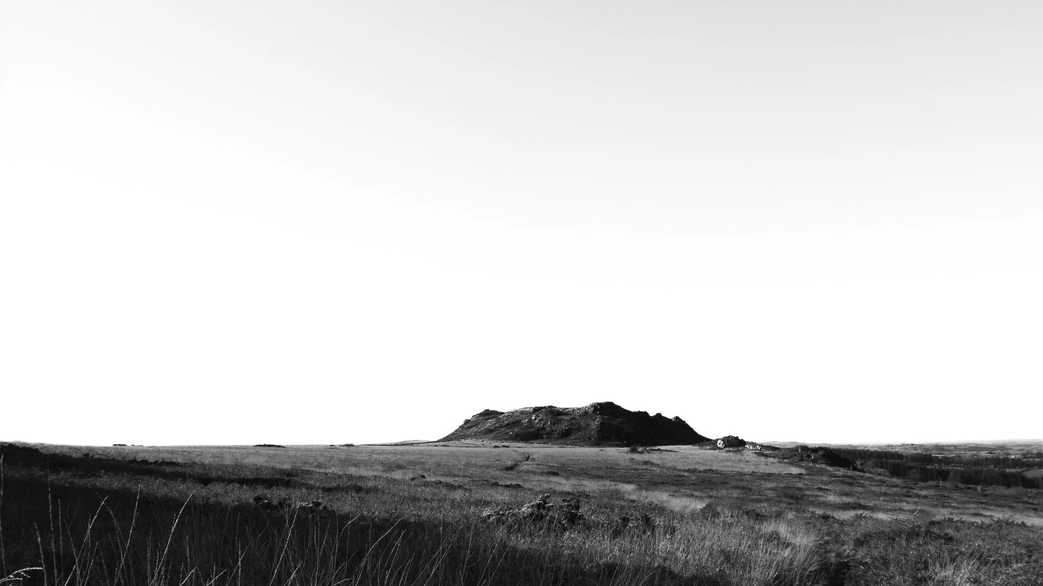 Paysage rural en noir et blanc avec une colline au centre et des champs ouverts autour.