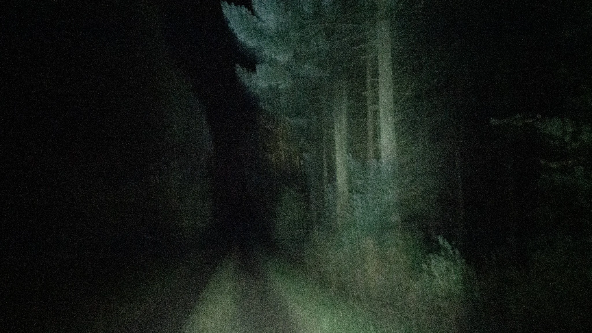 Une scène nocturne sombre avec peu de lumière, montrant probablement des bâtiments ou une structure en arrière-plan.